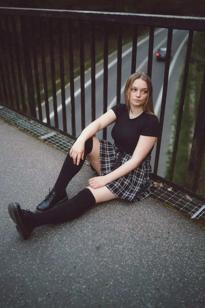 Dívka v kostkované sukni sedí na mostě