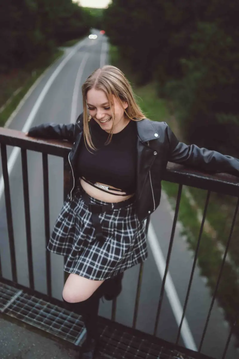 Dívka v kostkované sukni sedí na zábradlí mostu