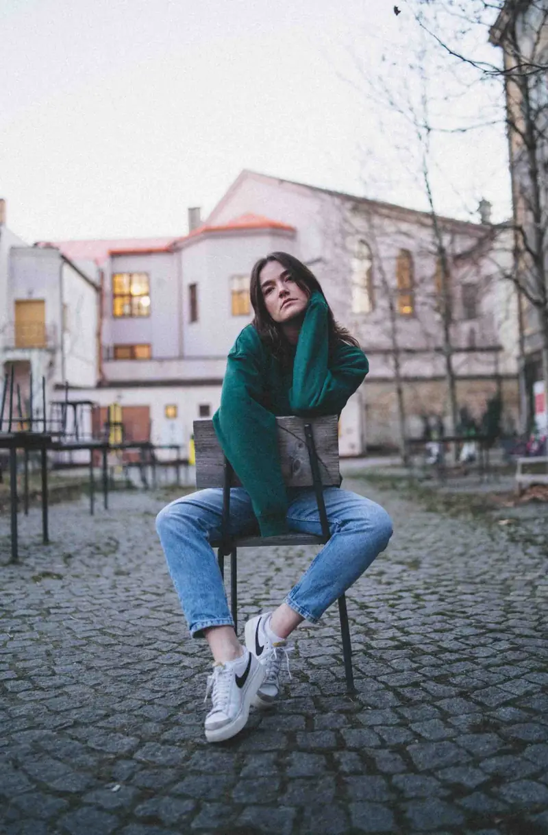 Žena v zeleném svetru na židli na dlážděné ulici