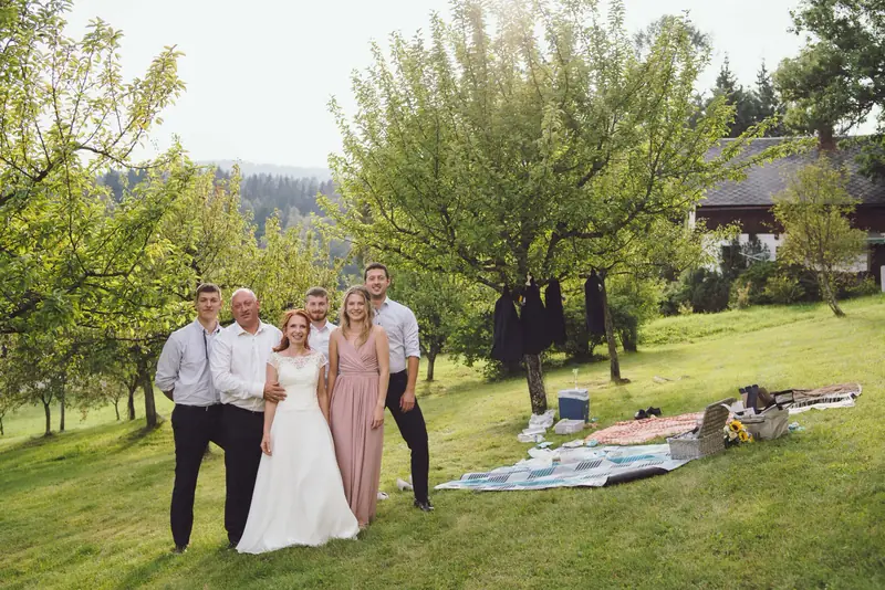 Novomanželé s rodinou na louce u piknikové deky