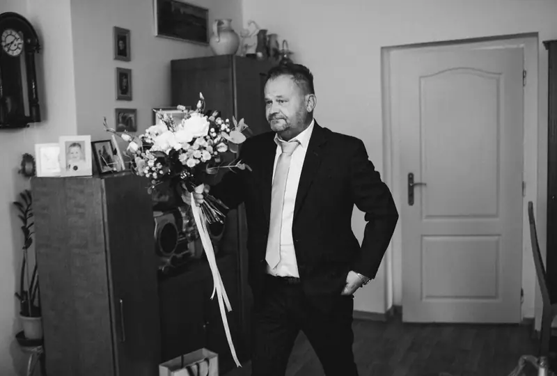 Černobílý snímek ženicha čekajícího doma s kyticí