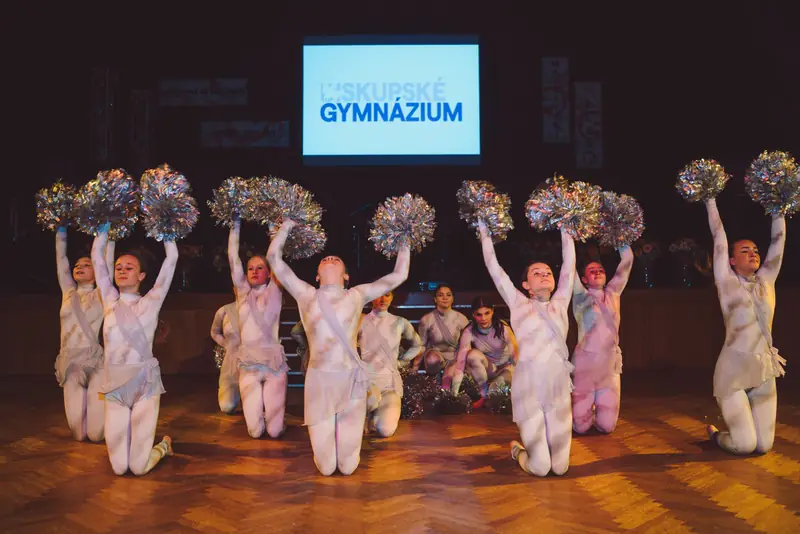 Maturantky s pompony na parketu před plátnem gymnázia