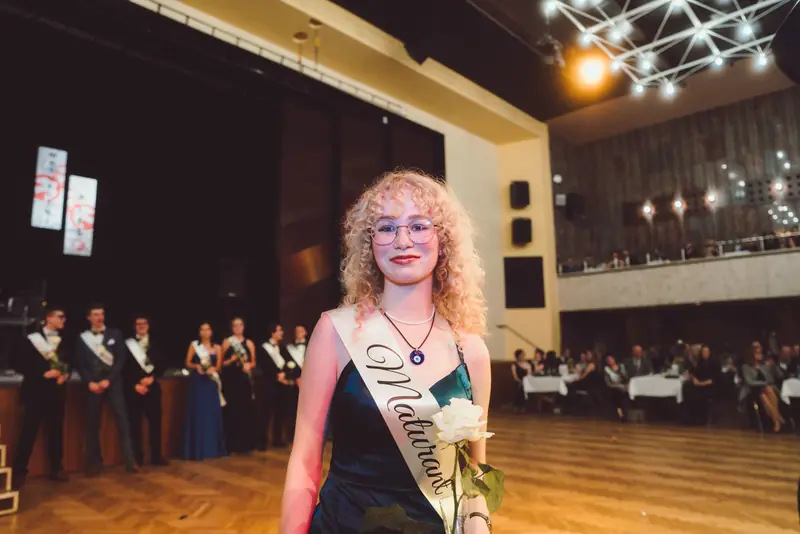 Maturantka se šerpou a květinou v sále