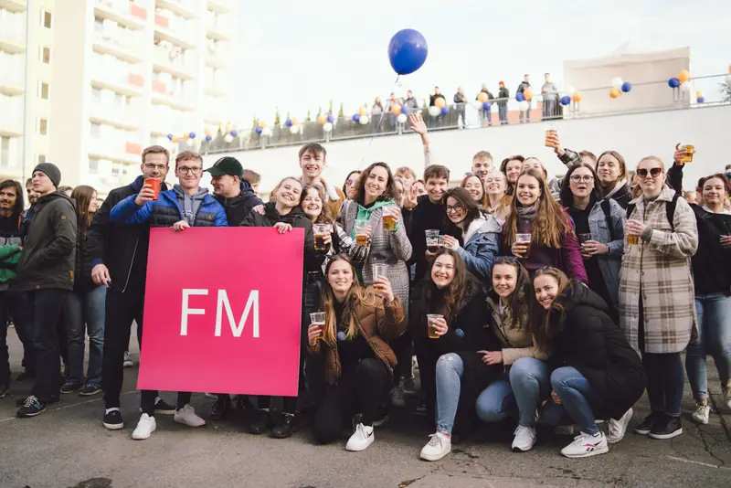 Skupina studentů s cedulí FM na kampusu
