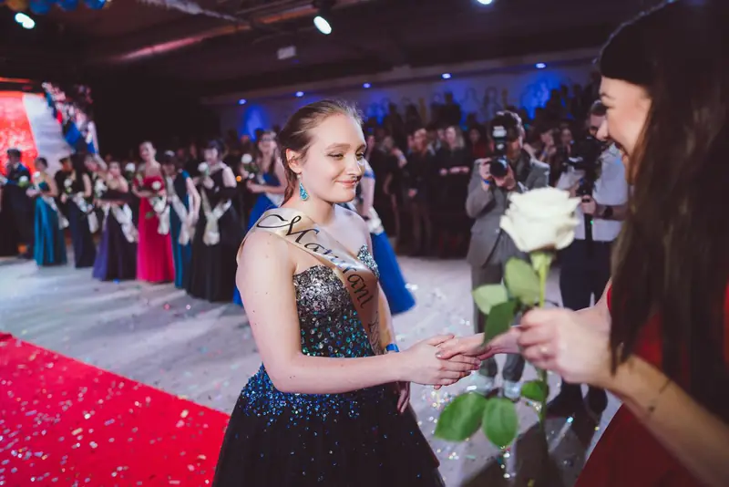 Maturantka přebírá bílou růži na červeném koberci