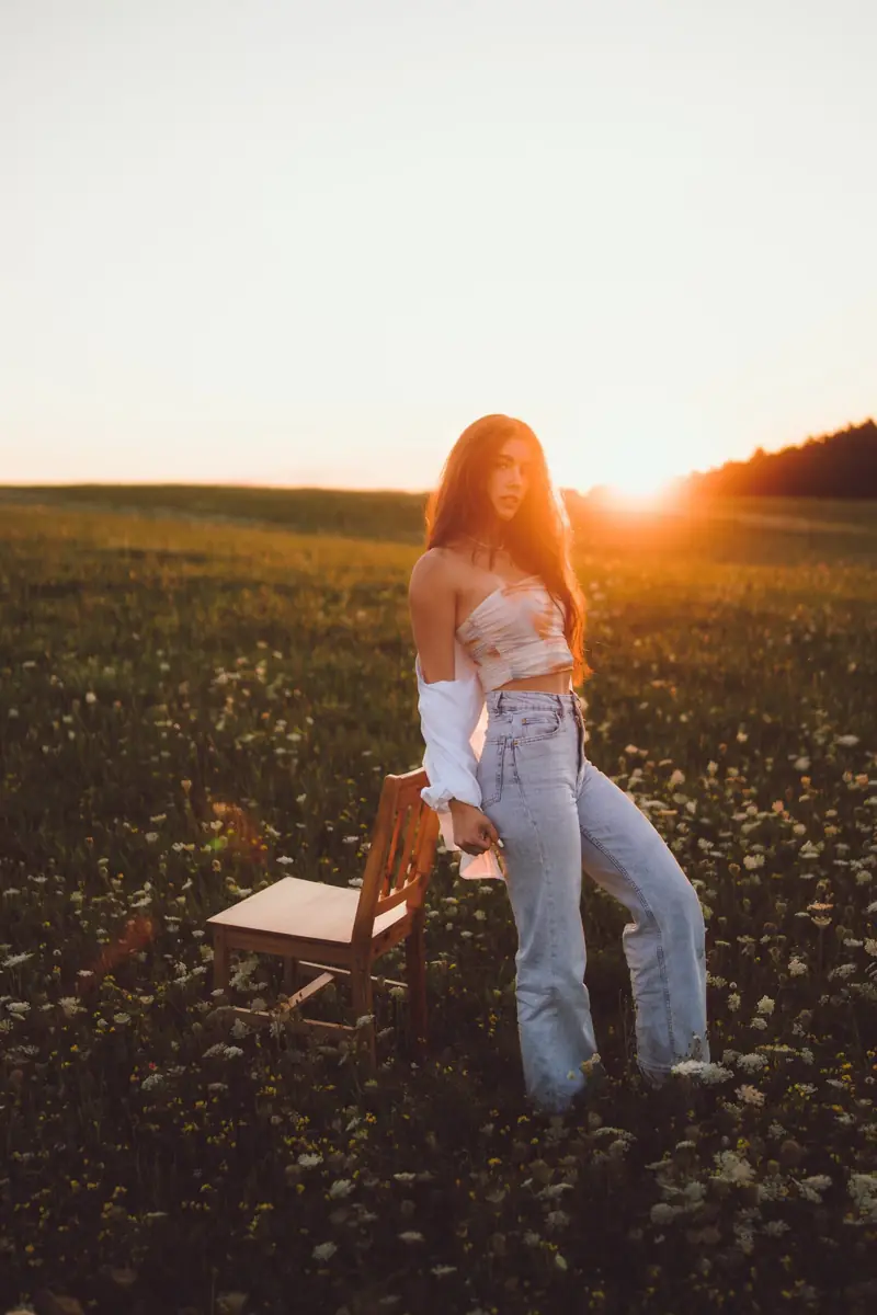 Dívka stojí u židle na louce při západu slunce