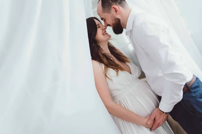 Partner se sklání k těhotné ženě u závěsu
