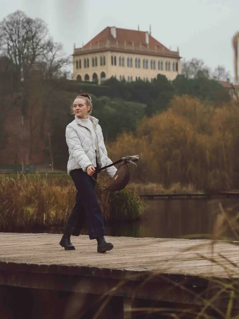 Modelka s taškou kráčí po molu, v pozadí zámek